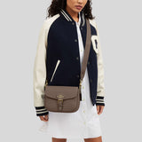 Person wearing a navy and white varsity jacket with a brown bag on a light gray background